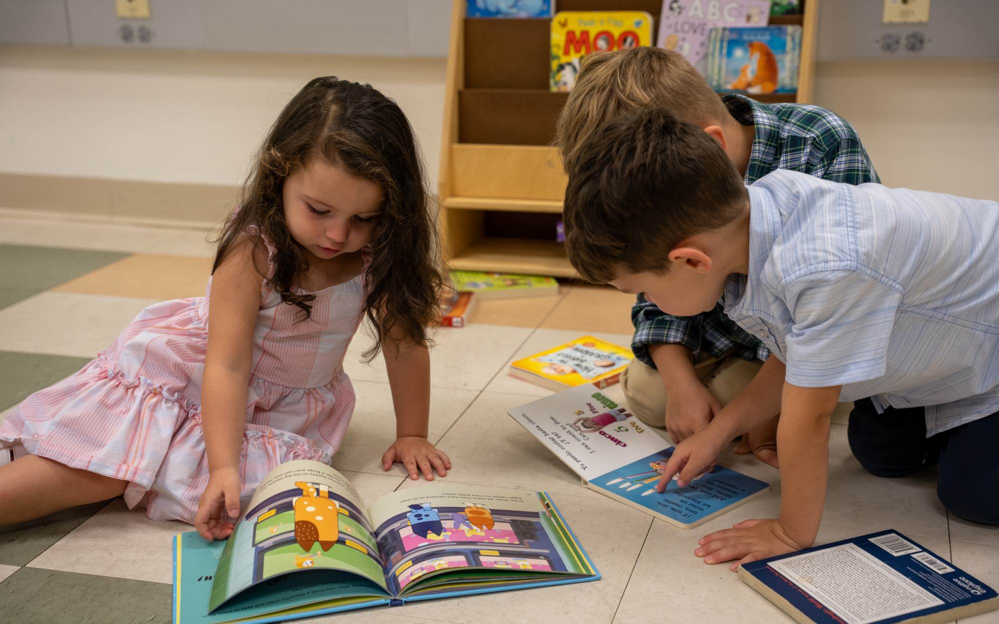 Three children reading picture books together on the classroom floor