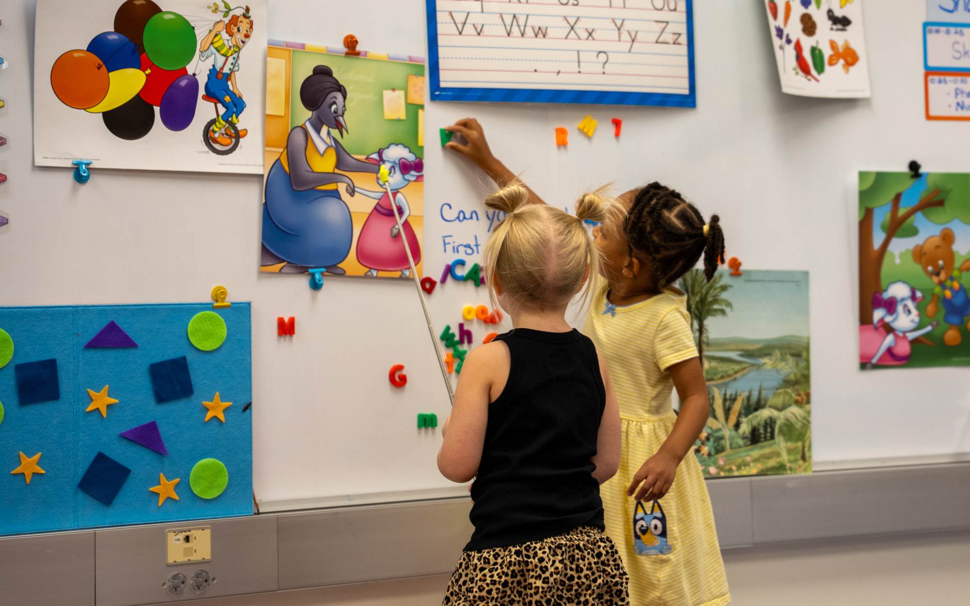 Two children reaching up to the alphabet board in their classroom