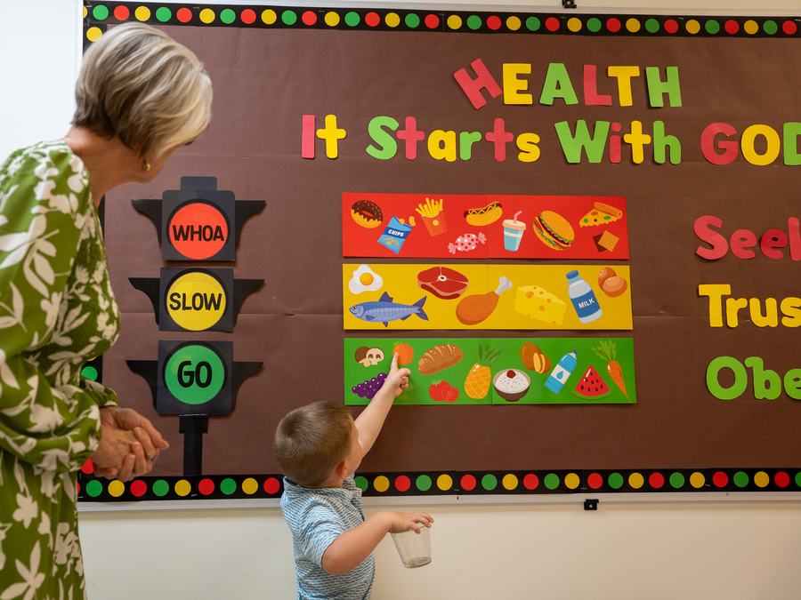 A toddler pointing at the healthy-food chart on the &ldquo;Health: It Starts With God&rdquo; bulletin board
