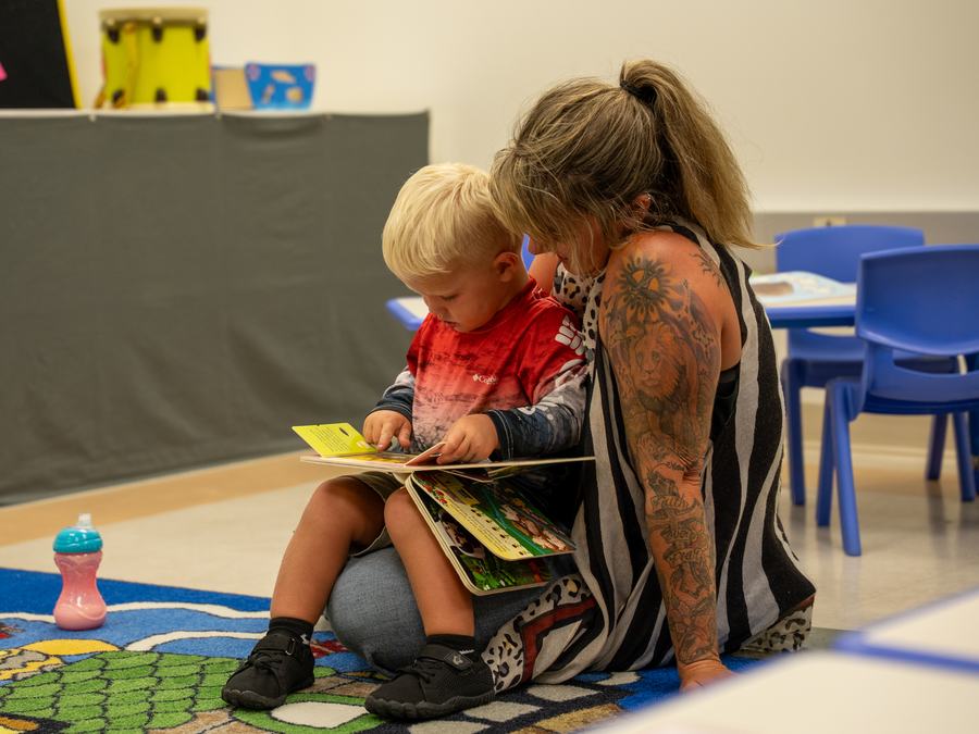A little boy looking through a picture book with a grown-up on the classroom rug