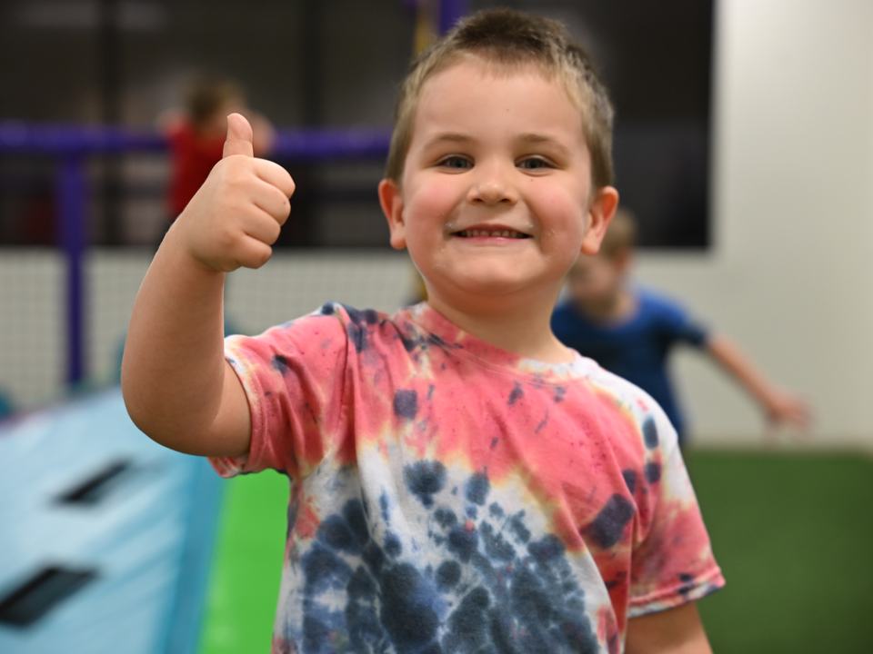 A grinning boy in a tie-dye shirt giving a thumbs up