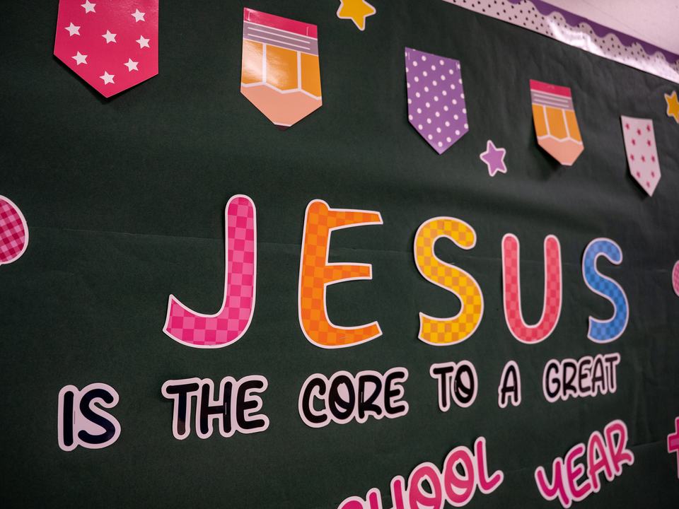 A classroom bulletin board with bunting and big checked letters reading “Jesus is the core to a great school year”