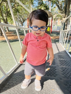 Santiago in blue glasses and a coral polo shirt, smiling on a playground walkway